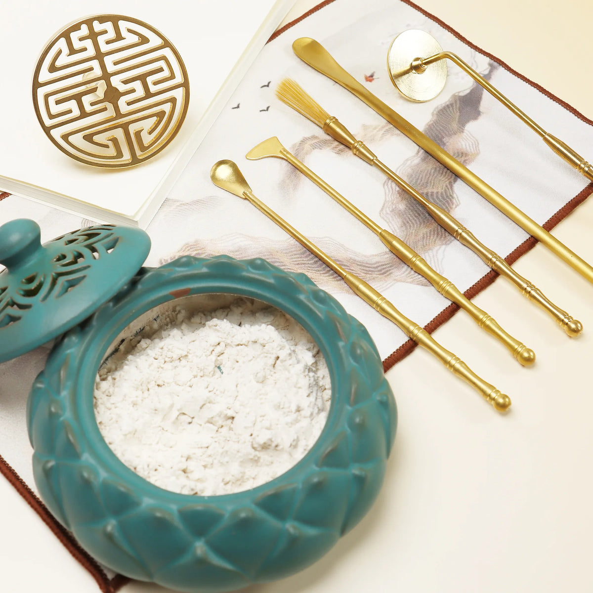 Turquoise ceramic seal mold with white powder and golden sealing tools arranged on fabric with decorative elements