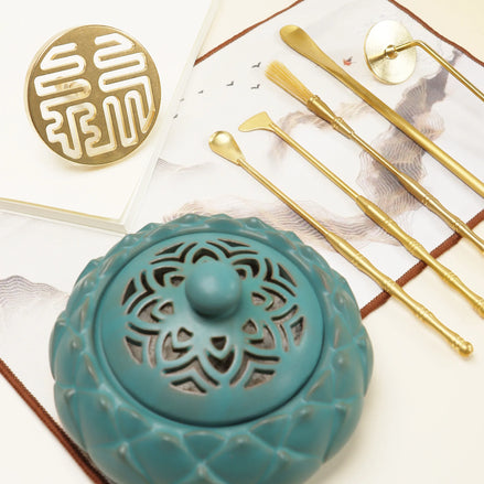 Turquoise ceramic incense holder with carved patterns, gold prosperity seal, and brass ritual tools on white surface