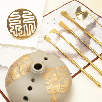 YUKI incense kit with ceramic burner featuring gold leaf pattern and set of golden sealing tools arranged on white surface