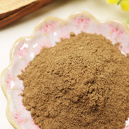 Fine brown incense powder displayed in decorative glass bowl with floral pattern on white surface