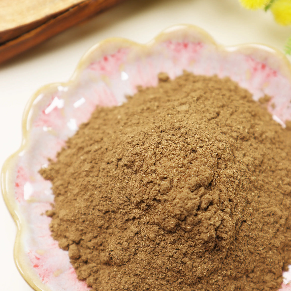 Fine brown incense powder displayed in decorative glass bowl with floral pattern on white surface
