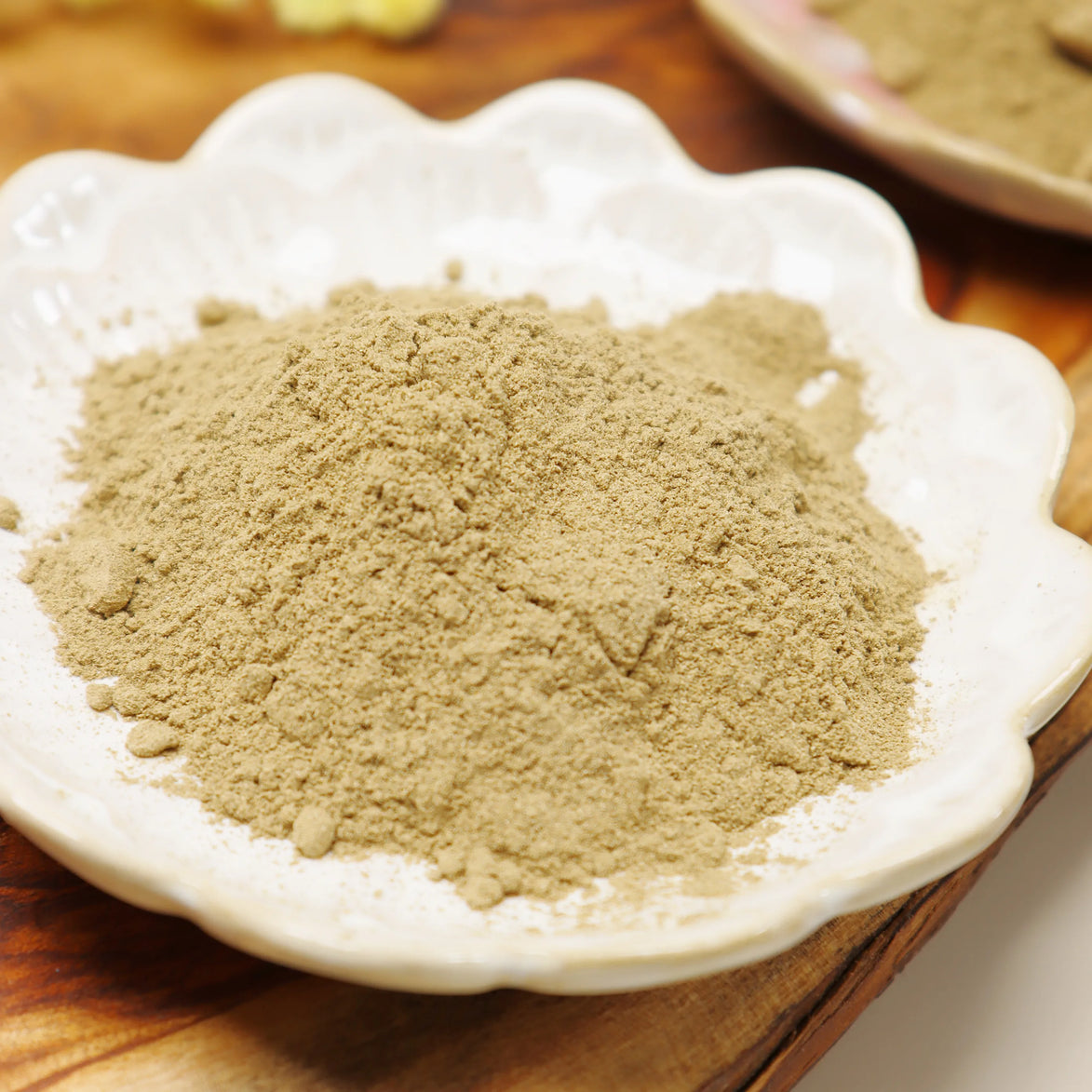 Fine beige herbal incense powder displayed in a white scalloped ceramic dish on wooden surface