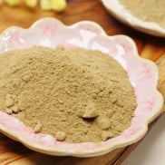 Fine brown incense powder in decorative pink floral ceramic dish on wooden surface with ginger in background
