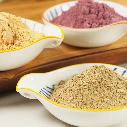 Three white ceramic bowls with yellow trim containing different colored natural incense powders on wooden surface