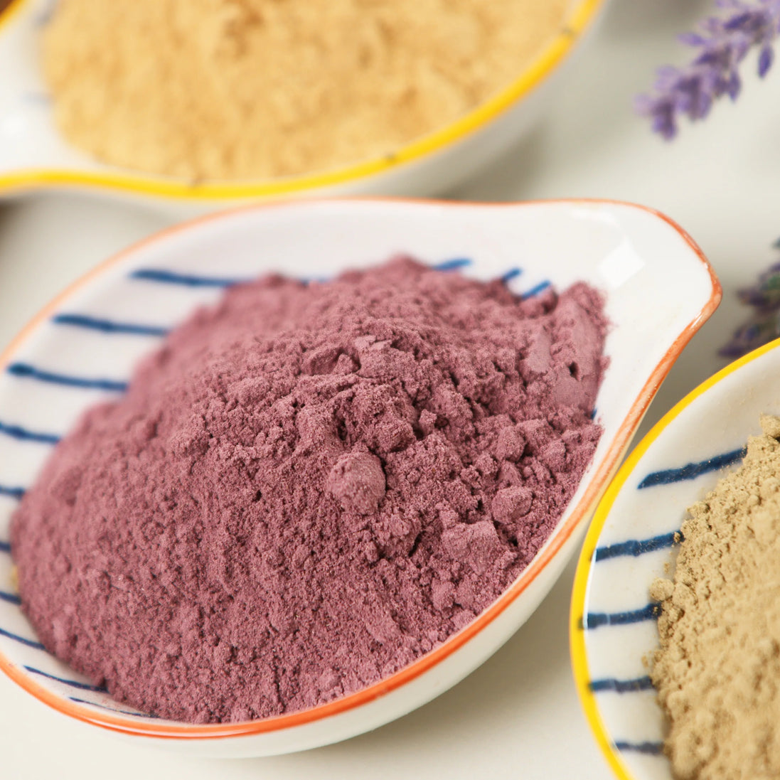 Purple-pink natural incense powder in striped ceramic bowl alongside other colorful incense blends