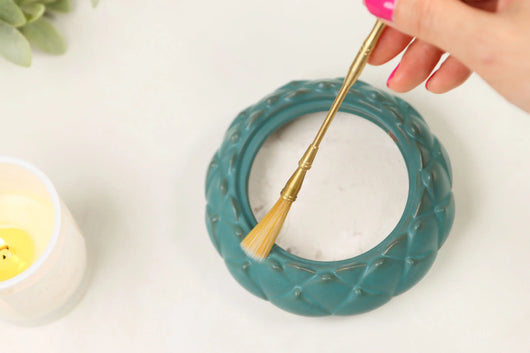 Brass-handled brush with natural bristles held over teal ceramic incense burner with decorative twisted pattern