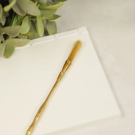 Brass incense brush with natural bristles and decorative metal handle on white marble surface with green plant