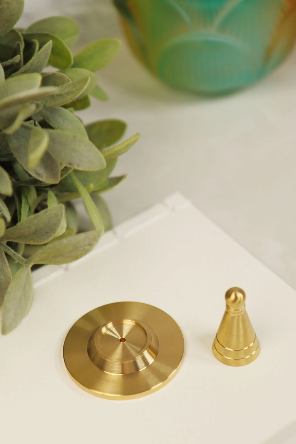 Golden copper incense cone maker with heavy circular base and pointed cone piece displayed on white marble surface