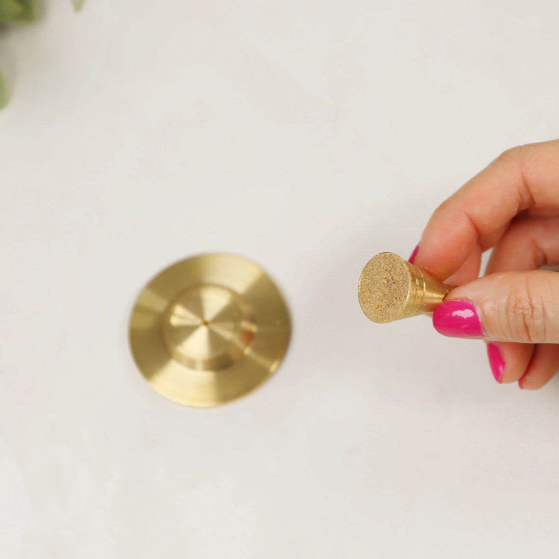 Hand holding golden copper incense cone tool with matching base plate on white surface