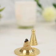 Copper-colored incense cone on brass holder with gold incense tools in soft-focused background