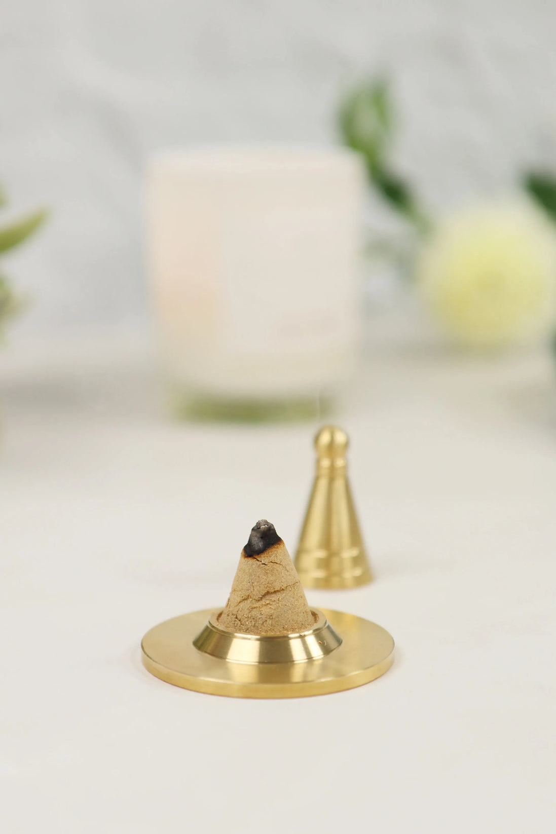 Copper-colored incense cone on brass holder with gold incense tools in soft-focused background