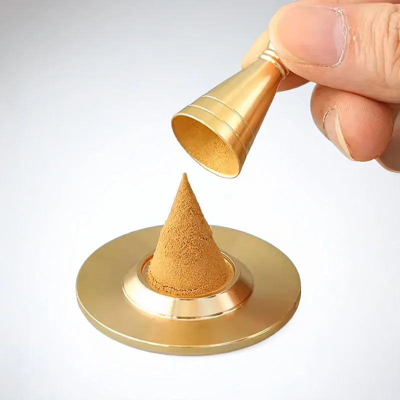 Hand holding gold copper cone maker pouring powder onto circular base forming cone shape