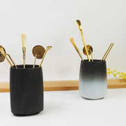 Matte black and ombre ceramic holders containing gold-toned sealing tools and implements on wooden display
