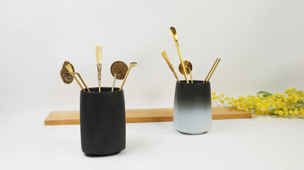 Matte black and ombre ceramic holders containing gold-toned sealing tools and implements on wooden display
