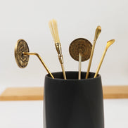 Black ceramic holder with brass incense tools, wax seals, and ornate implements on wooden surface