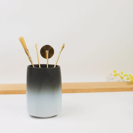 Ombre ceramic holder in black to white gradient with gold brass tools and brush on wooden shelf
