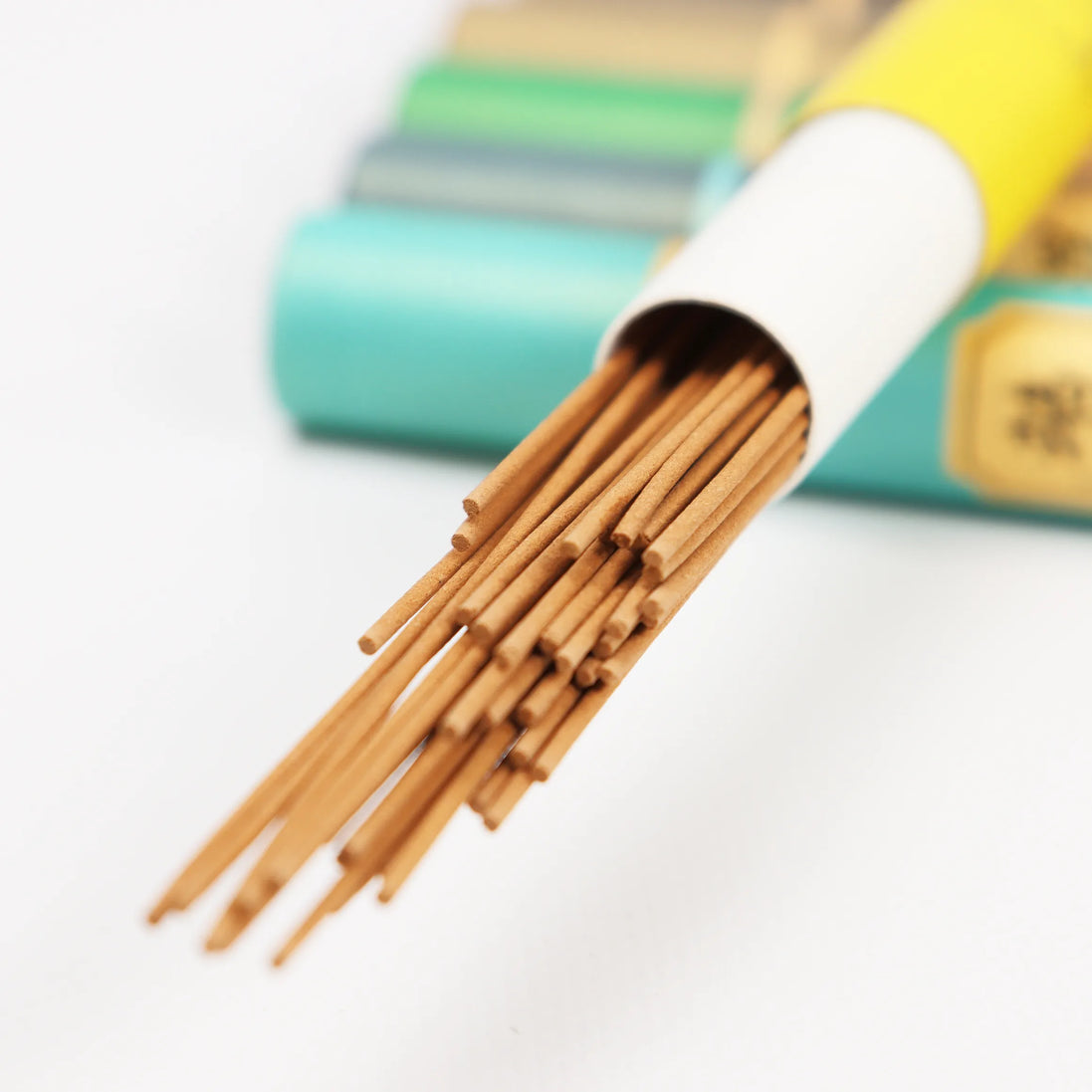 Natural incense sticks displayed in white ceramic holder with turquoise packaging in background