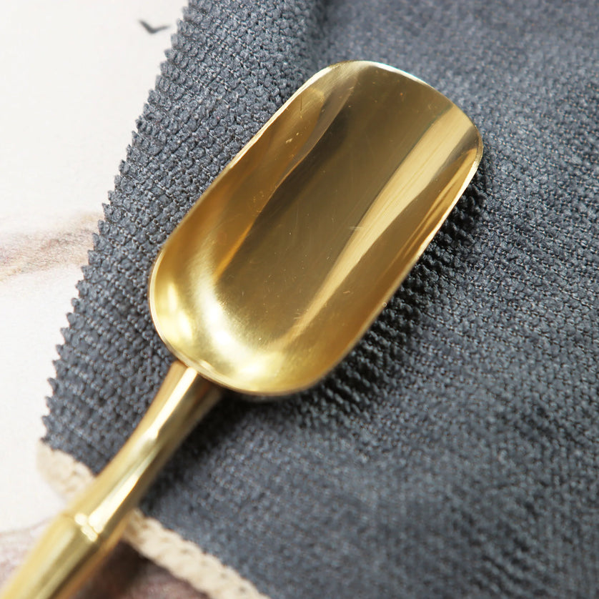 Golden brass spoon being polished with dark textured microfiber cleaning cloth on gray surface