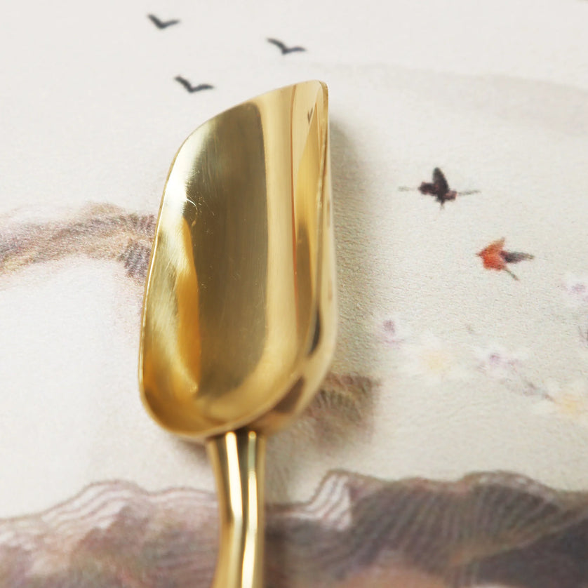 Golden brass polishing cloth by Peoni & Stone with artistic background featuring flying birds and landscape