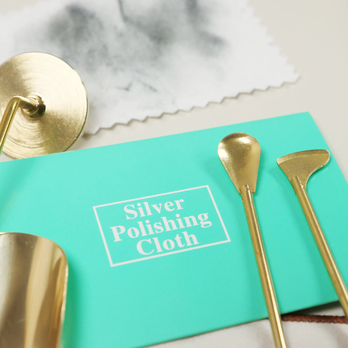 Turquoise Peoni & Stone silver polishing cloth surrounded by golden brass tools and decorative items on marble surface