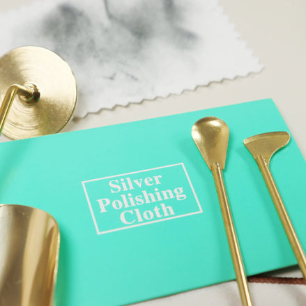 Turquoise Peoni & Stone silver polishing cloth surrounded by golden brass tools and decorative items on marble surface
