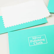 Turquoise silver polishing cloth with white text label on cream background, serrated edges visible