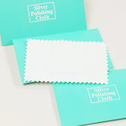 White microfiber polishing cloth with zigzag edges displayed with turquoise packaging labeled Silver Polishing Cloth