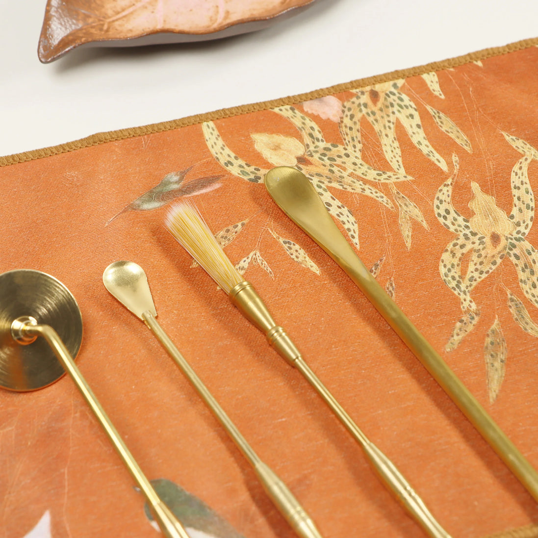Orange suede ceremony cloth with decorative pattern and gold ritual tools arranged on surface