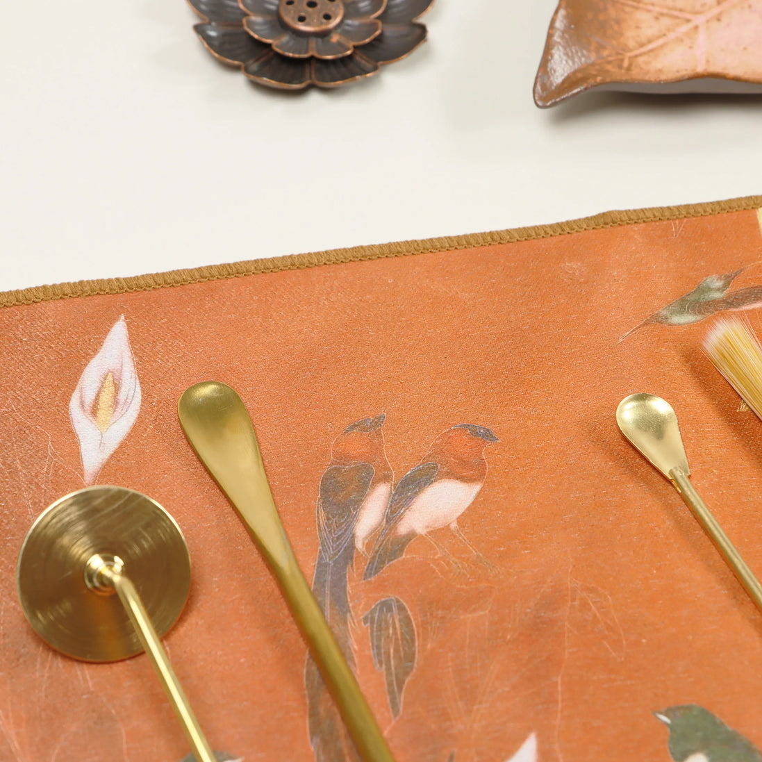 Coral orange suede ritual cloth with botanical leaf design and brass ceremonial tools arranged on surface