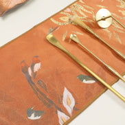 Orange suede ritual cloth with floral pattern and gold brass ceremonial tools arranged on surface