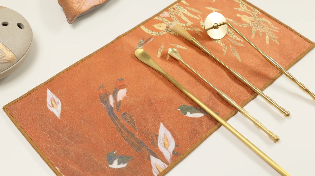 Orange suede ritual cloth with floral pattern and gold brass ceremonial tools arranged on surface