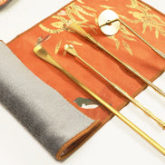 Orange suede ritual cloth with golden tea tools displayed on top, showing traditional ceremony accessories