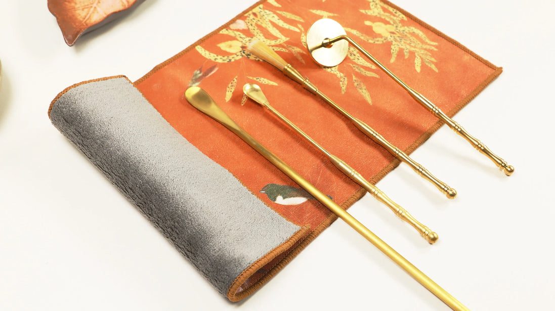 Orange suede ritual cloth with golden tea tools displayed on top, showing traditional ceremony accessories