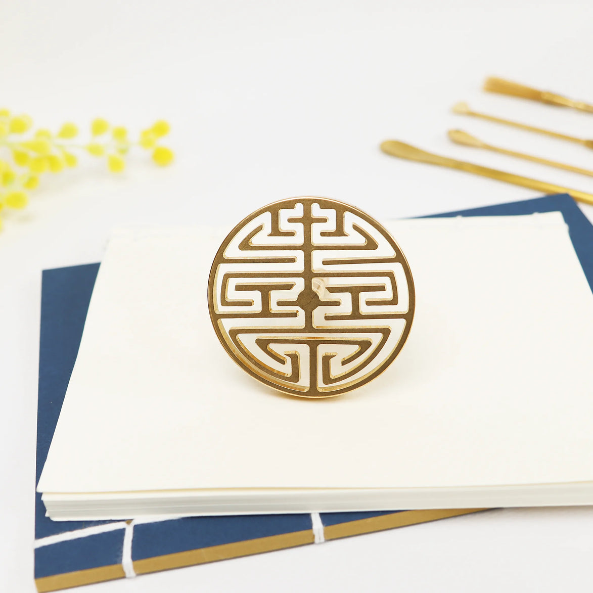 Circular brass seal with Chinese double happiness symbol in geometric cutout pattern on white surface
