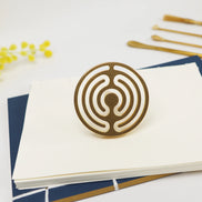 Brass circular seal with concentric labyrinth pattern displayed on white cards with gold office supplies