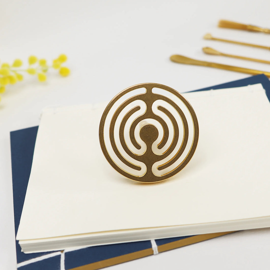 Brass circular seal with concentric labyrinth pattern displayed on white cards with gold office supplies