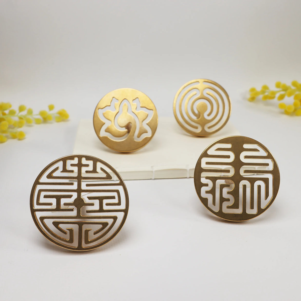Four circular brass incense seals with lotus flower and geometric cutout patterns on white surface