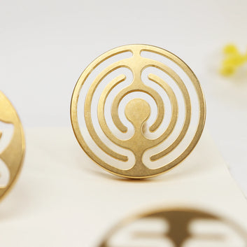 Brass circular seal with concentric labyrinth pattern standing upright on white surface