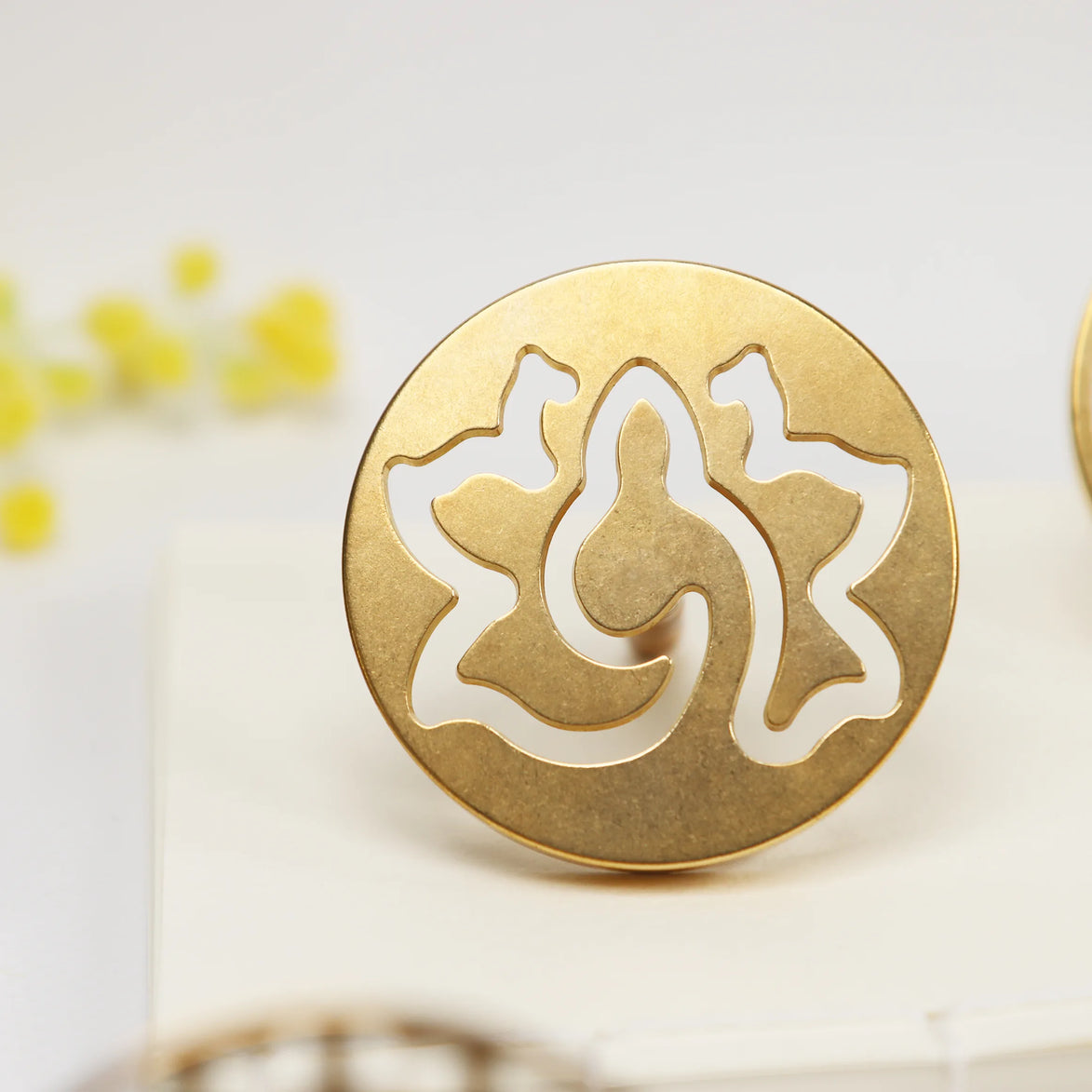 Round brass seal with cut-out lotus flower design standing upright on white surface