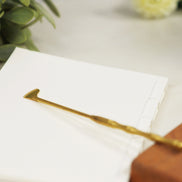 Golden brass incense spade tool with flat blade resting on white surface next to plant