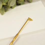 Golden brass spade tool with flat angled head and long handle on white marble surface with eucalyptus leaves