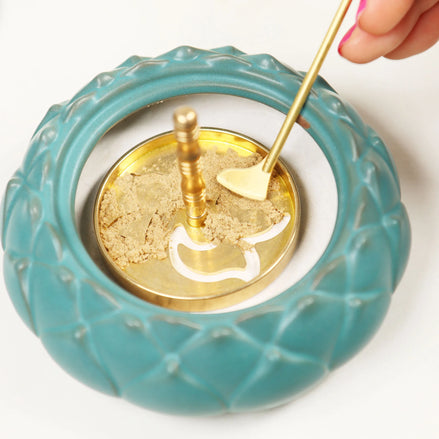 Brass incense spade tool smoothing powder in turquoise ceramic incense seal with gold center and decorative rim