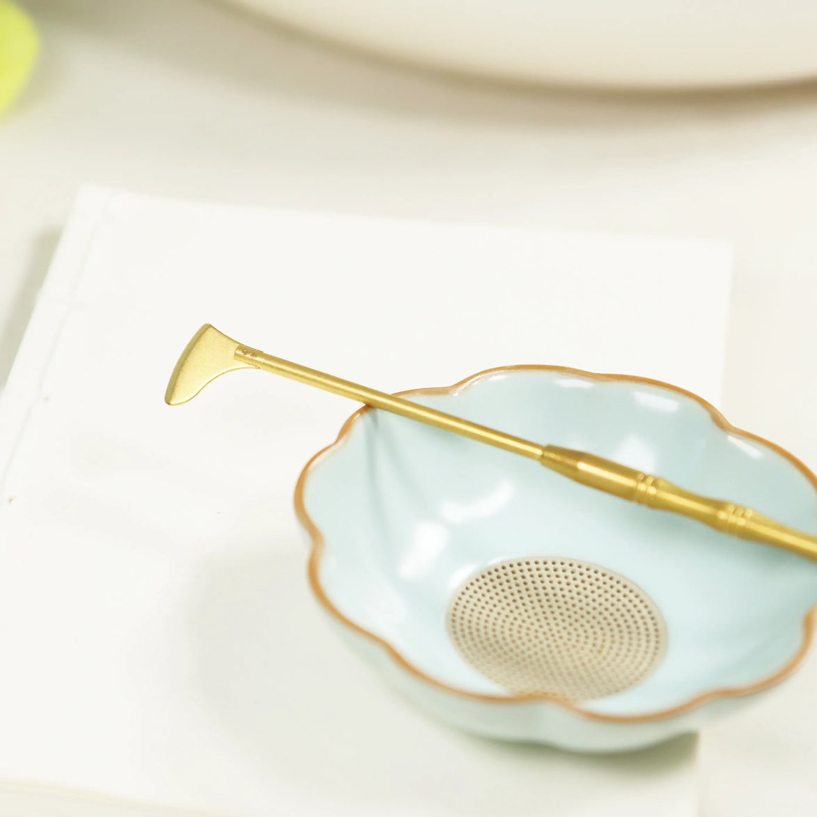 Brass incense sealing spade with flat blade resting on mint green scalloped ceramic dish