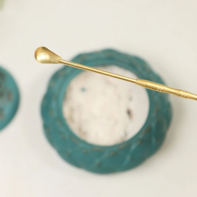 Golden brass spoon with long handle and rounded bowl for scooping incense powder, displayed on white surface