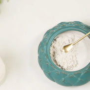 Brass incense spoon scooping white powder from turquoise ceramic bowl with textured rim pattern