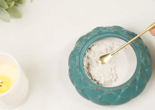 Brass incense spoon scooping white powder from turquoise ceramic bowl with textured rim pattern