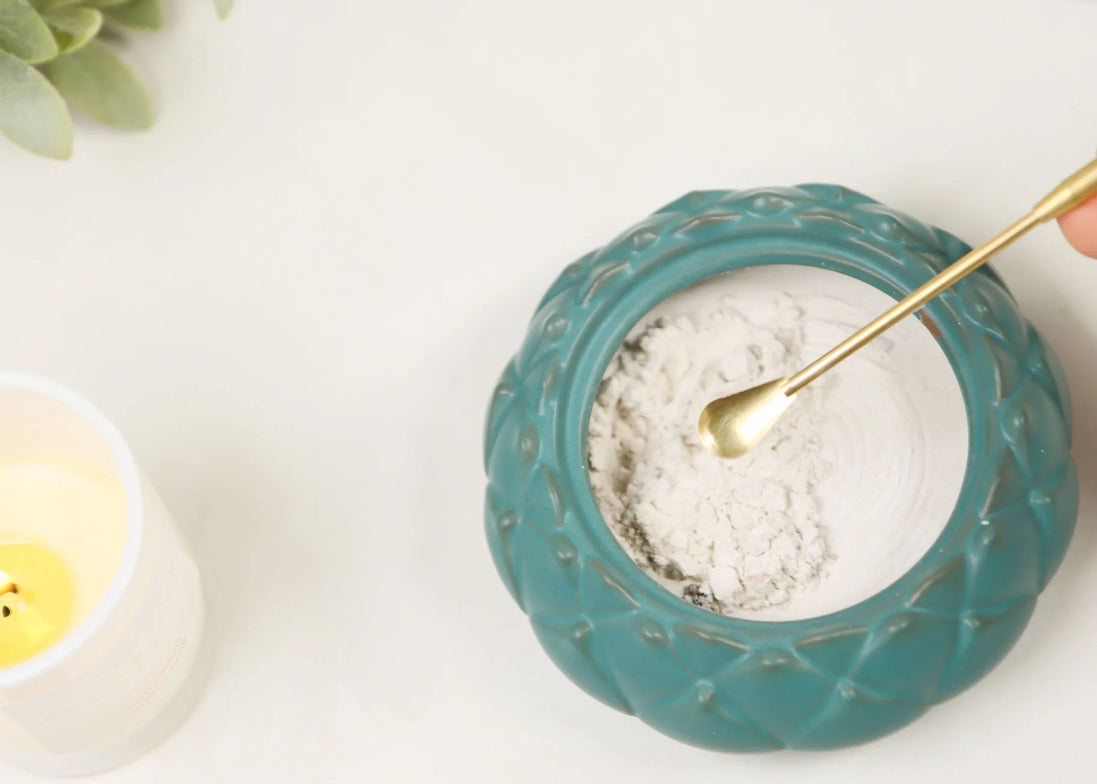 Brass incense spoon scooping white powder from turquoise ceramic bowl with textured rim pattern