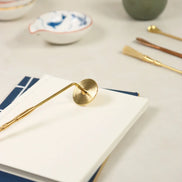 Golden brass incense sealing stamp with circular head resting on white paper beside ceramic bowls and green jar