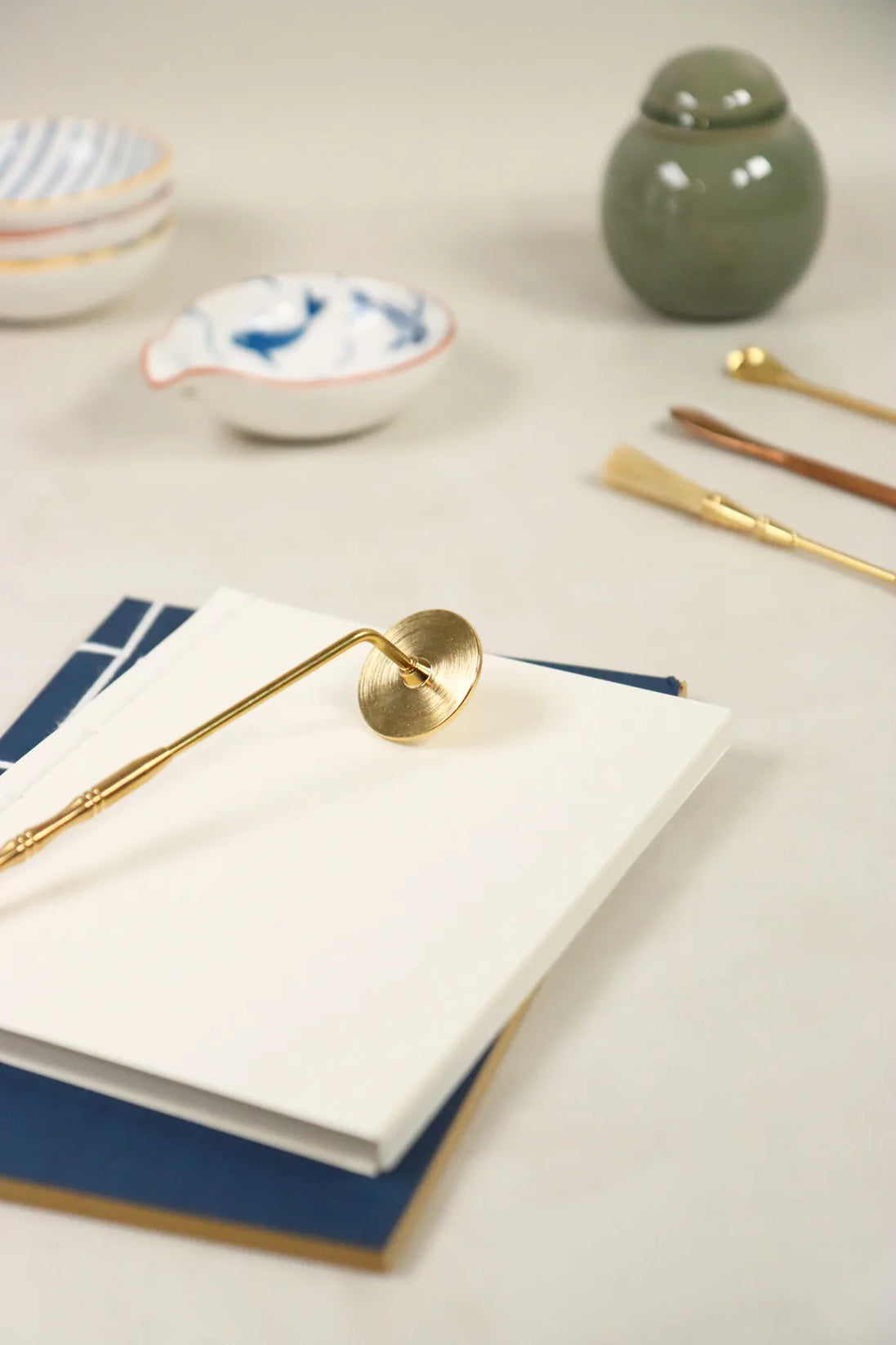 Golden brass incense sealing stamp with circular head resting on white paper beside ceramic bowls and green jar