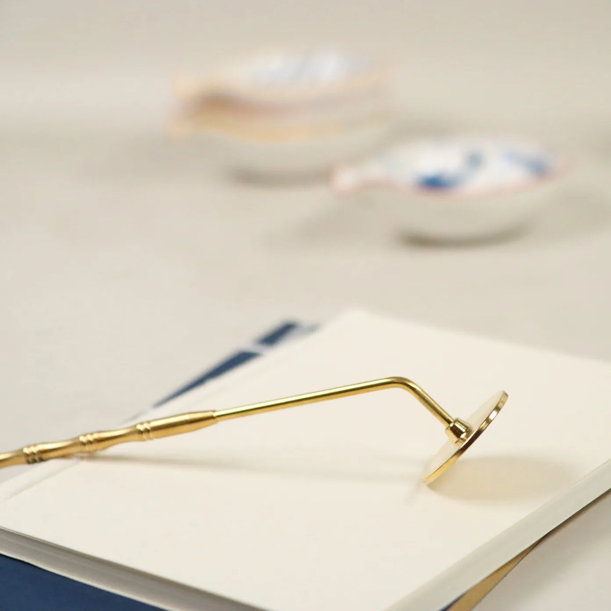 Gold brass incense sealing tool with curved handle resting on white surface for smoothing ash powder beds